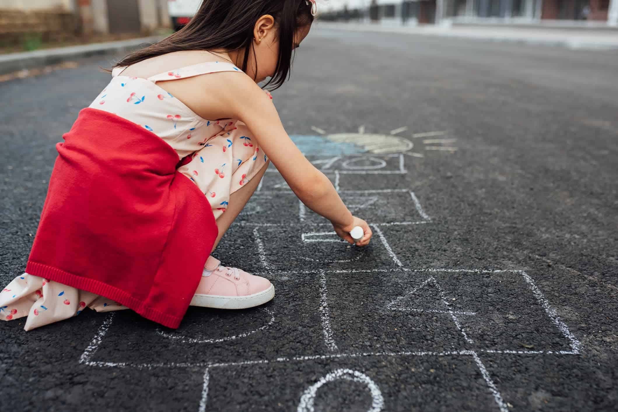 a girl playing and drawing hopscotch in the playground with chalk